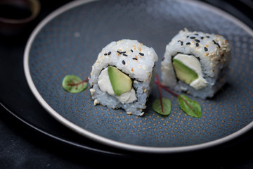 avocado and cream cheese inside out maki sushi wuth sesame seeds on dark plate with chopsticks and soy sauce