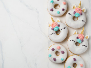 Fototapeta na wymiar Unicorn donuts over white marble background. Trendy donut unicorn with white glaze. Top view or flat lay. Copy space for text.