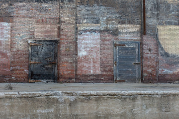 Two large metal doors attached to an abandoned crumbling red brick warehouse