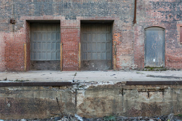 Large vintage metal doors on the back of an abandoned crumbling red brick warehouse