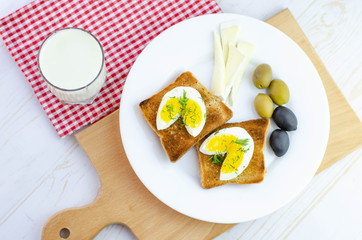Fresh toast with eggs, olives and soy cheese  for breakfast and glass of milk on white wooden background with wooden cutting board and checkered towel. Healthy vegetarian food concept