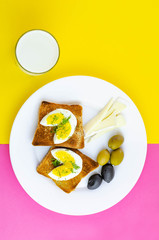 Fresh toast with eggs, olives and soy cheese  for breakfast and glass of milk with on pink and yellow background. Healthy vegetarian food concept
