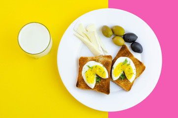 Fresh toast with eggs, olives and soy cheese  for breakfast and glass of milk with on pink and yellow background. Healthy vegetarian food concept