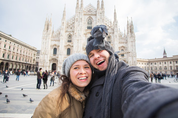 Fototapeta na wymiar Travel, Italy and funny couple concept - Happy tourists taking a self portrait with pigeons in front of Duomo cathedral, Milan