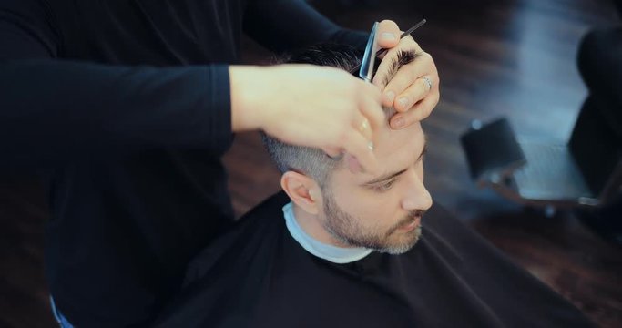 Hairdresser cuts quiff on a man with gray hair. Stylist works with scissors and a comb. Close-up.