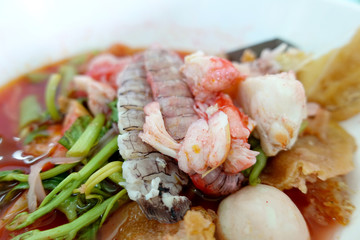 Yentafo Spicy noodle soup,hot and spicy ,with mix seafood, crayfish, shrimp. Asian spicy seafood noodle soup in white bowl on table background. Thai style noodle and street food of Thailand.
