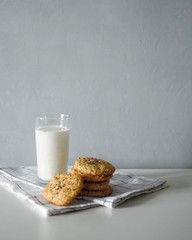 Glass of milk with homemeade ginger oatmeal cookies with white towel on grey background.