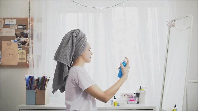 Young woman with towel spraying micellar water on face