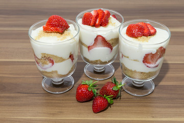 layered dessert or Magnolia with strawberries, biscuit cake and cream cheese on a white wood background.
