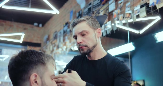 Brutal barber cuts a man's bang at a hair salon. Portrait view.