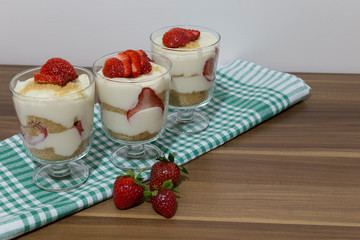 layered dessert or Magnolia with strawberries, biscuit cake and cream cheese on a white wood background.