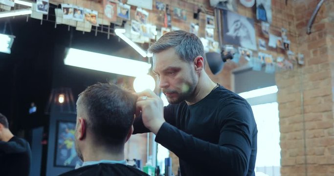 Professional hairdresser cuts the client in the barber shop. Stylist works with scissors.