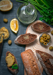 A composition of two baguettes of bran and whole grain flour. Sandwich of hummus and olives. A vessel with vegetable oil. On a wooden spread. View from above.