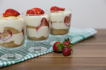 layered dessert or Magnolia with strawberries, biscuit cake and cream cheese on a white wood background.