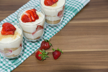layered dessert or Magnolia with strawberries, biscuit cake and cream cheese on a white wood background.