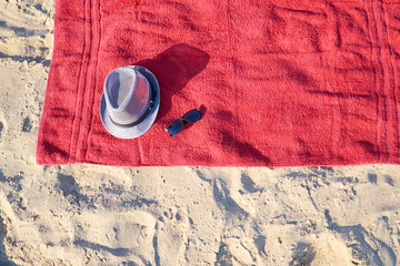 Red terry towel on light background with hat and sunglasses, top view