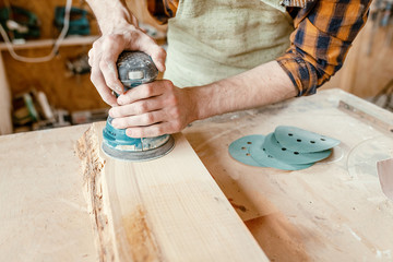man works in the shop and polishes a wooden board using grind machine. The concept of manual labor