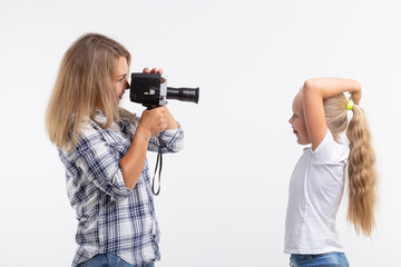 People, photography and hobby concept - woman using an old fashioned camera and photographing a little girl on white background