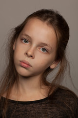 Obraz premium Portrait of an eight-year-old girl with a calm mood, in a black blouse and with picked up hair. Studio photo session. Gray background