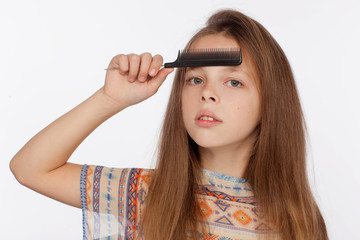 Obraz premium Portrait of an eight-year-old girl who is combing her hair with a comb. Studio photo shoot on a white background