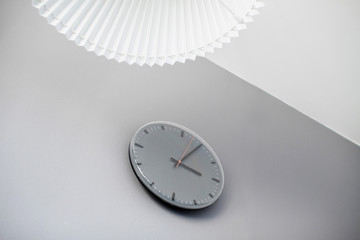 Minimalistic view of the clock and lampshade on the gray wall. Textured background in gray-white tone with copy space