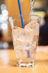 Pouring water with ice cubes on wooden table at restaurant. 
