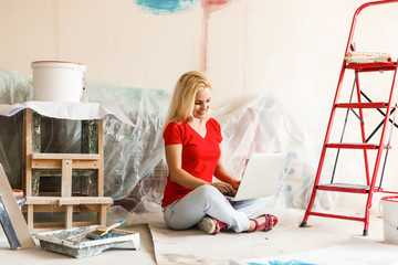 Young woman portrait while painting new apartment ,sitting with laptop. Young woman with laptop
