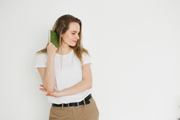 Portrait of succesful smiling woman in casual wear with green book on light background.