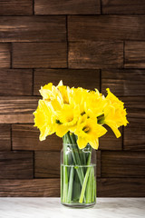 Spring yellow Daffodils flowers in vase, on wooden background