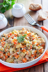 Russian salad in spanish with canned tuna on a white plate on a wooden table, horizontal