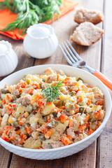 Russian salad in spanish with canned tuna on a white plate on a wooden table, horizontal