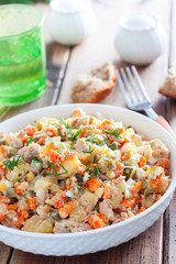 Russian salad in spanish with canned tuna on a white plate on a wooden table, horizontal