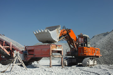 Obraz premium Heavy red excavator and mobile gravel sorter installation against the background of gravel hills and blue sky. Quarry equipment. Mining industry.
