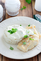 Fried cod, cooked with rice and cream sauce on a white plate, selective focus