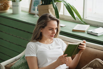 Beautiful woman in casual wear reading green book on sofa.