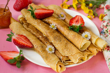 Stack of thin pancakes served with strawberries and daisy flowers