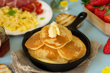 Pancakes with butter served with scrambled eggs and ham for breakfast