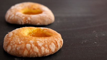 Two doughnuts with powdered sugar and apricot jam lay on the table one by one. Delicious fresh pastry will be an addition to tea or coffee in a friendly company.