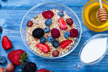 Greek yogurt granola and berry mix. Top view. Delicious healthy muesli with raspberry, blueberry, strawberry, hazelnut, BlackBerry, milk and honey on blue wooden rustic table
