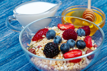 Delicious healthy muesli with raspberry, blueberry, strawberry, BlackBerry, hazelnut, milk and honey on blue wooden rustic table. homemade muesli or granola with honey, milk, fresh berries and nuts