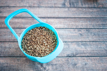 Dry buckwheat in a color container on a wooden table, space for text