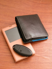 Man accessories: leather wallet, smart phone, and car key on a wooden surface.