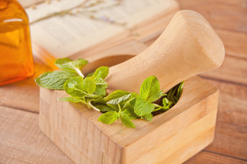 Fresh mint, wooden mortar, pestle,small bootle with mint oil and old book on the old table.