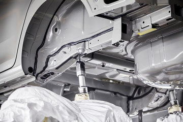 The robots in the car manufacturing plant are helping the car body to be glued at the seams.