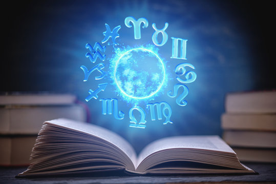 Open book on astrology on a dark background. The glowing magical globe with signs of the zodiac in the blue light