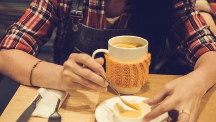 Girl tasting a dessert with tea with ginger and lemon in knitted cup in cafe.