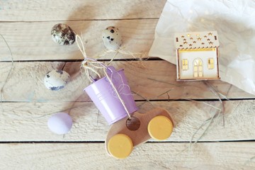 Toy car, quail eggs, a small house with illumination, on a light wooden table, top view, Easter concept