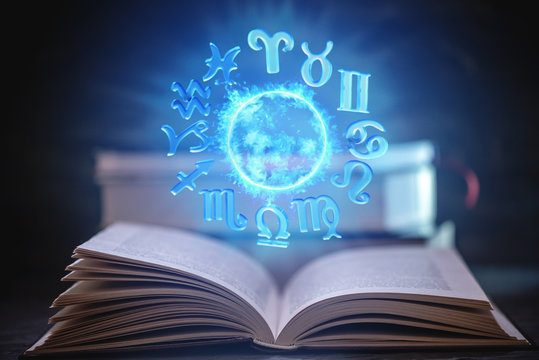 Open book on astrology on a dark background. Glowing magical globe with signs of the zodiac in the blue light.