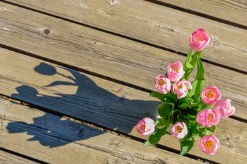 Fototapeta premium Vase of pink tulips on wooden deck with shadow