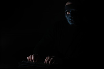 Fototapeta na wymiar A man in a mask prints on the keyboard in the dark